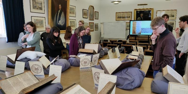 A group of researchers look at early modern books in a seminar room surrounded by portraits.