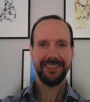 Photo of Gonzalo Rodriguez-Pereyra smiling to camera. Framed paintings are visible on the white wall behind him.