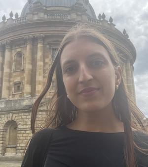 Head and shoulder shot of a woman wearing a black shirt standing in front of the Radcliffe Camera.