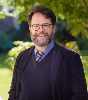 Photo of Dr Christoph Schmitt-Maass wearing a dark suit with blue and yellow tie. Bearded and wearing glasses, smiling at camera.